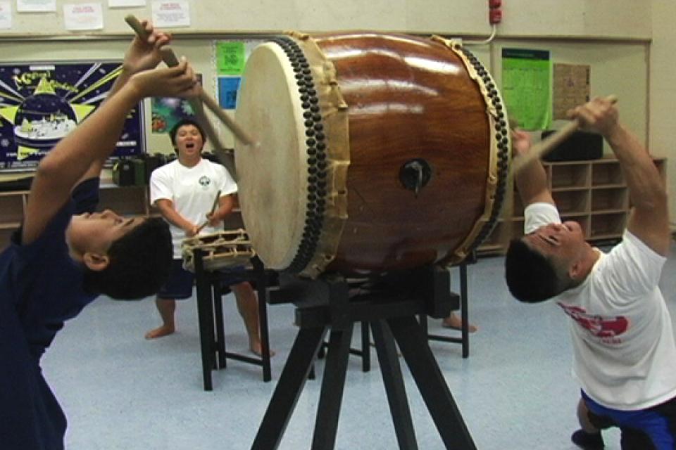 Two people bend back to beat the drum on either end